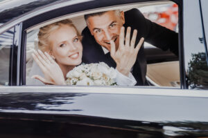 The newlyweds are showing their rings at the camera while sitting in the car.