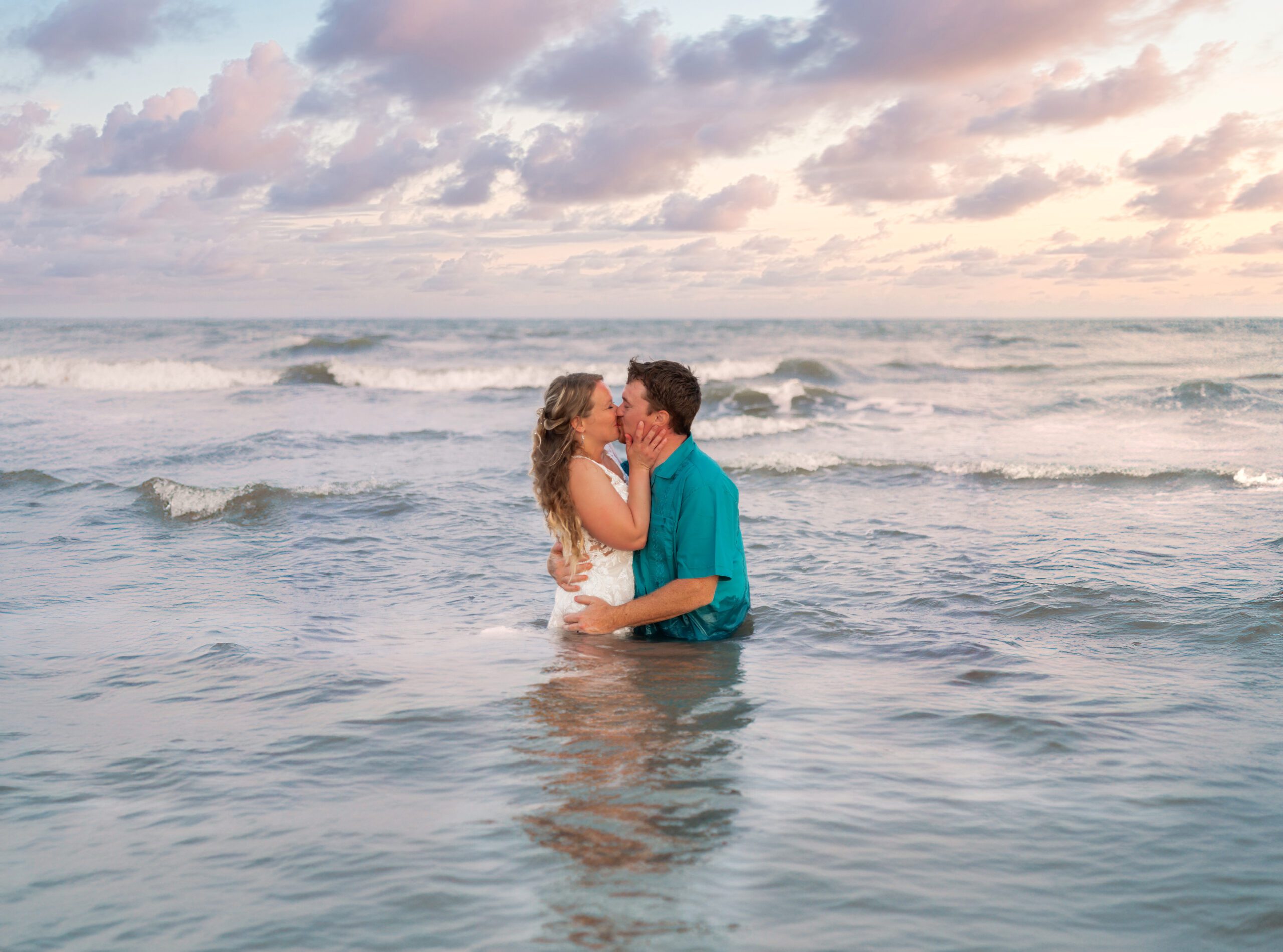 A bride and groom kiss in the water at sunset after their Wedding In Galveston.